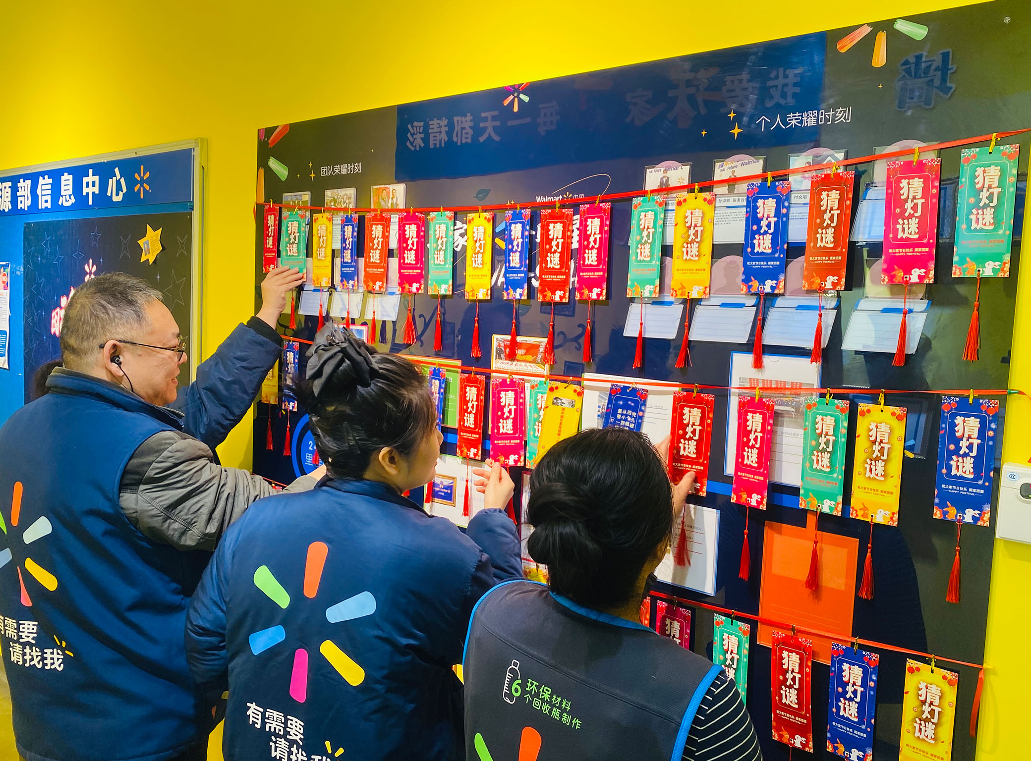 Four Walmart associates turn over colorful riddle cards hanging from the wall — part of their store’s Lunar New Year decor.