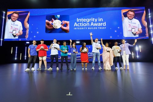 A diverse group of people stand on a large stage celebrating the Integrity in Action Award. 