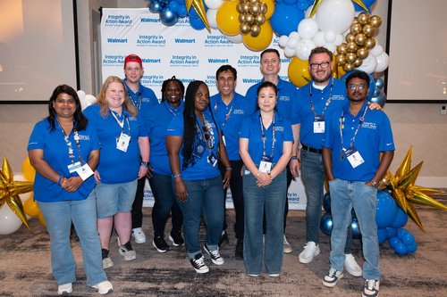 A diverse group of employees in blue Walmart shirts pose together for a group photo at the Walmart Integrity in Action Award celebration.