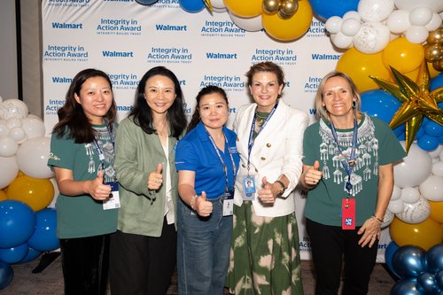 Five adults stand together in front of an Integrity in Action Award backdrop, smiling and giving thumbs up. 