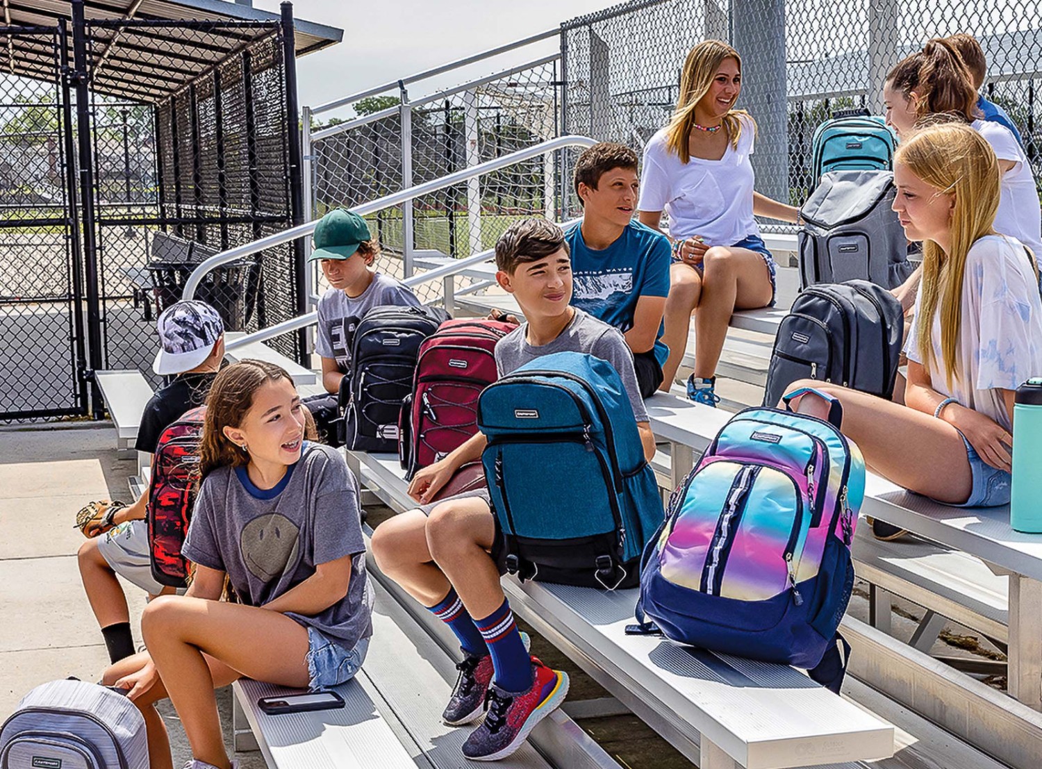 Students sit on baseball bleachers, comparing their new backpacks.
