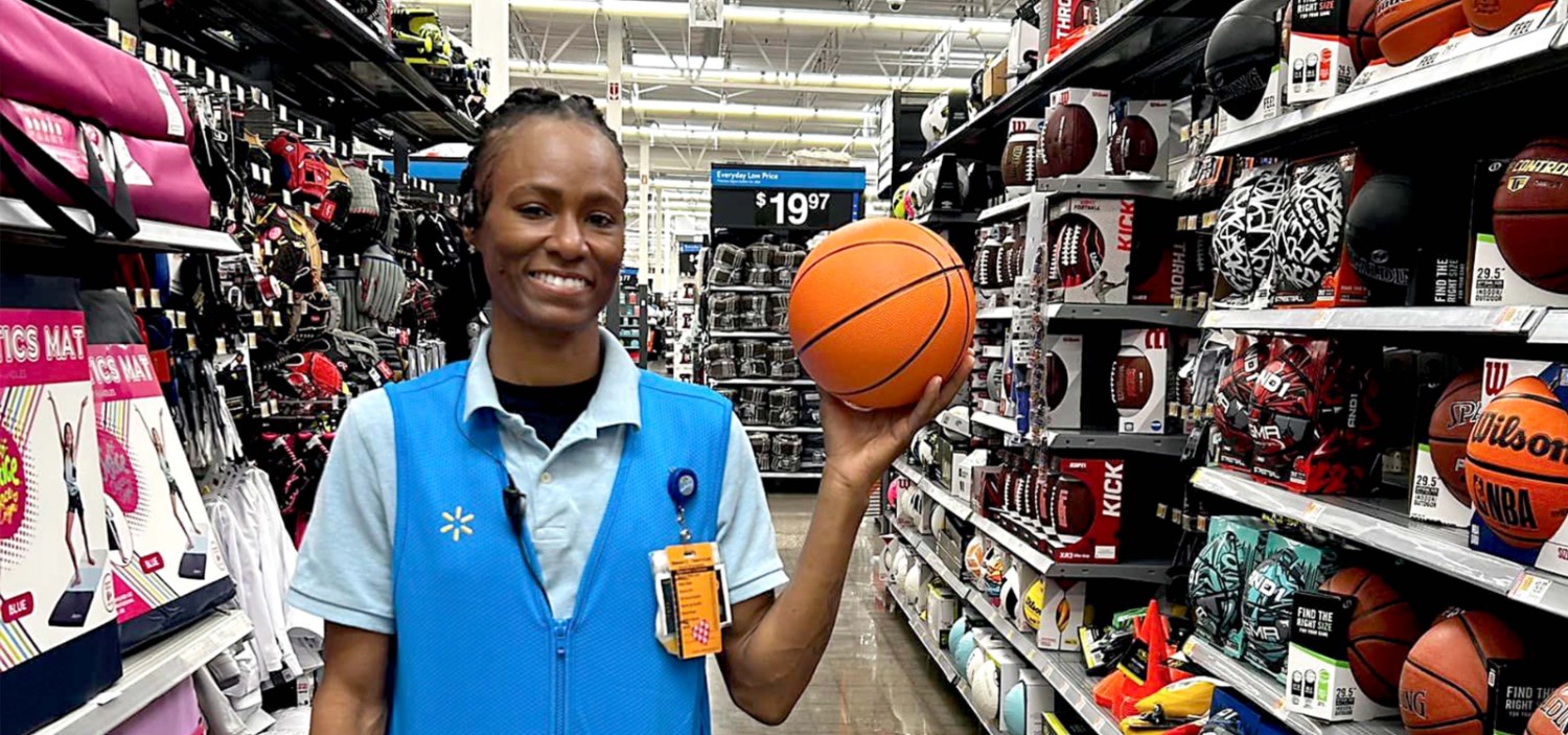 Crystal standing in front of the sport aisle of a Walmart store holding a basketball