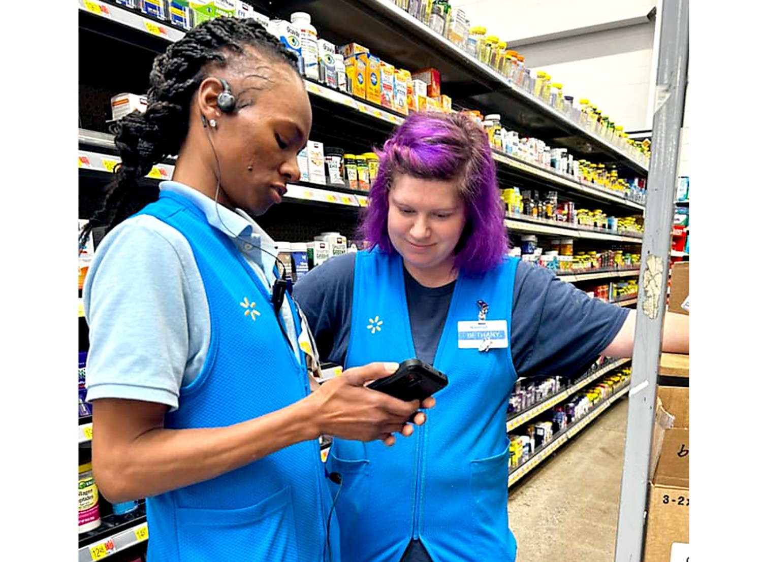Two female associates looking at a phone in the supplement aisle of a Walmart store