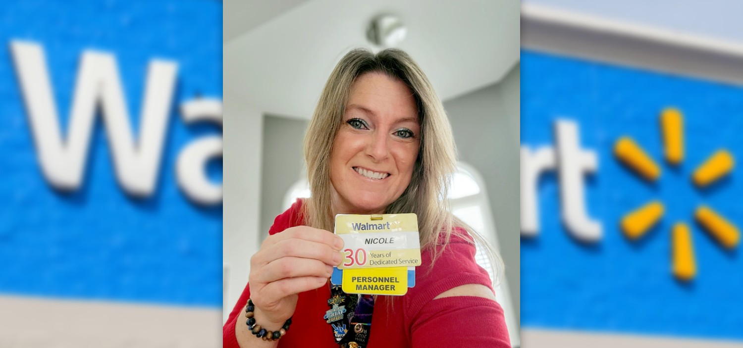 Nicole Lockyer holding up her 30 year associate badge with a Walmart super center store front background
