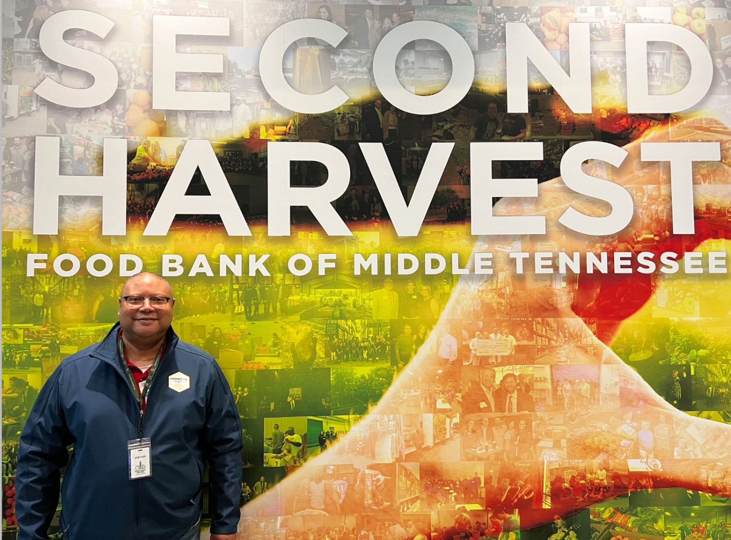 male associate standing in front of a colorful mural that reads "second harvest food bank of middle tennessee""