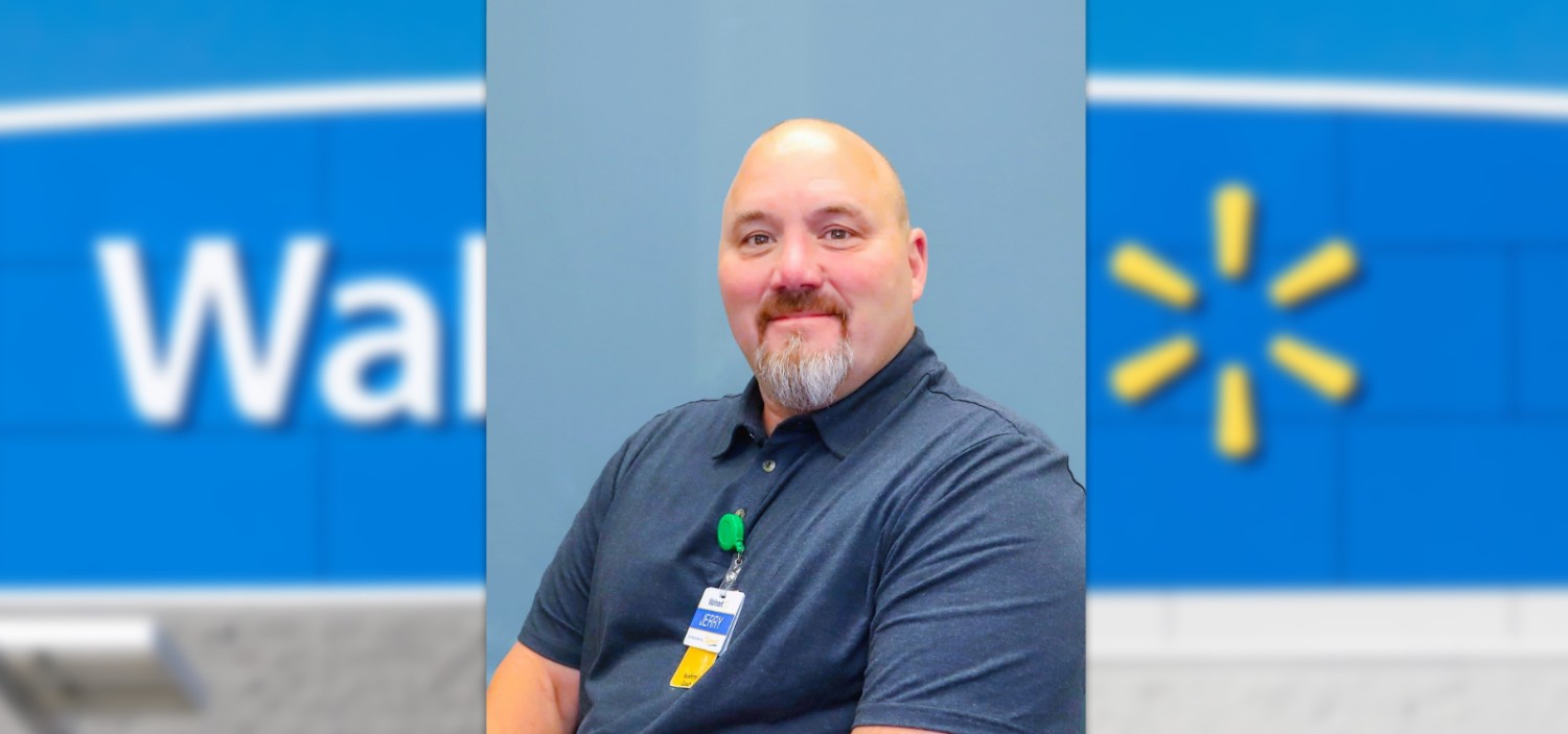 Male associate smiling at the camera with a Walmart store sign as the background