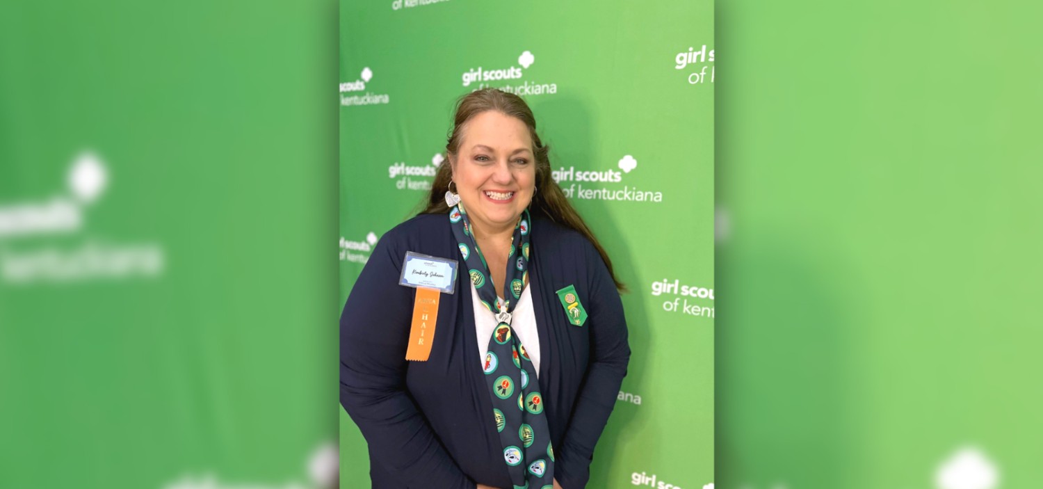 female associate smiling at the camera in front of a green girl scouts background
