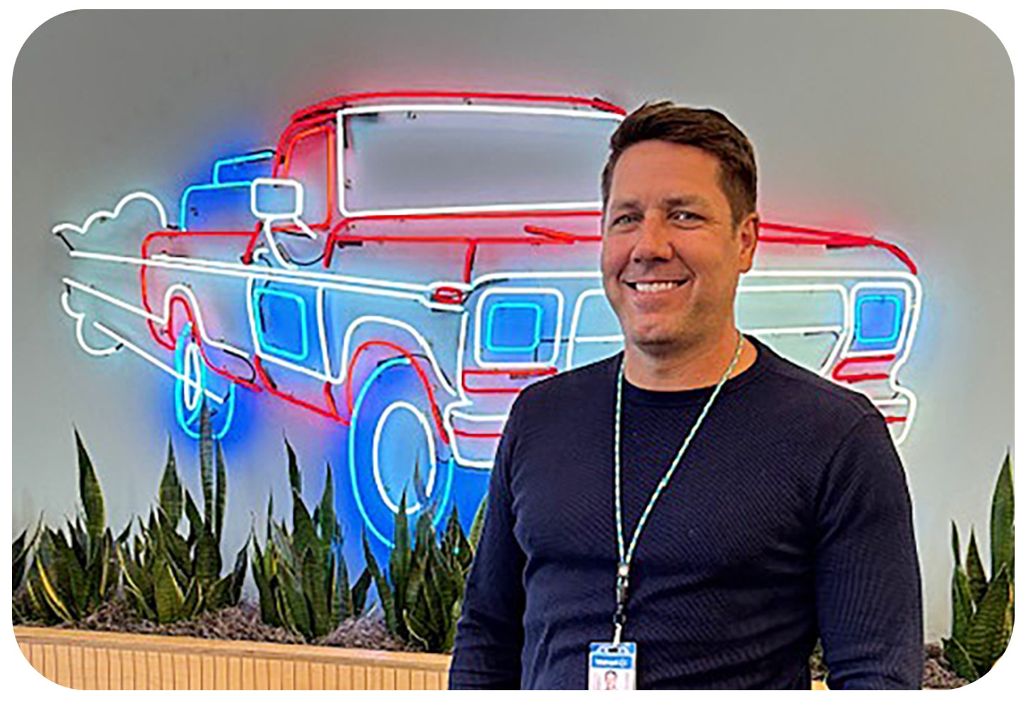 Walmart associate Gary Olsen poses in front of a neon sign of Mr. Sam's Ford truck at the home office.