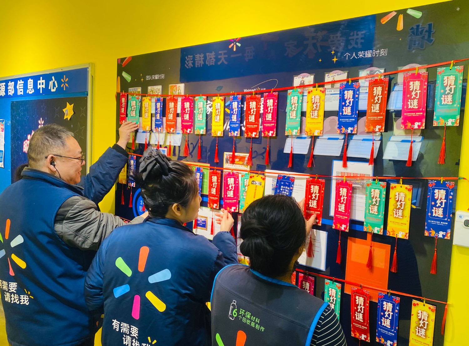 Four Walmart associates turn over colorful riddle cards hanging from the wall — part of their store’s Lunar New Year decor.