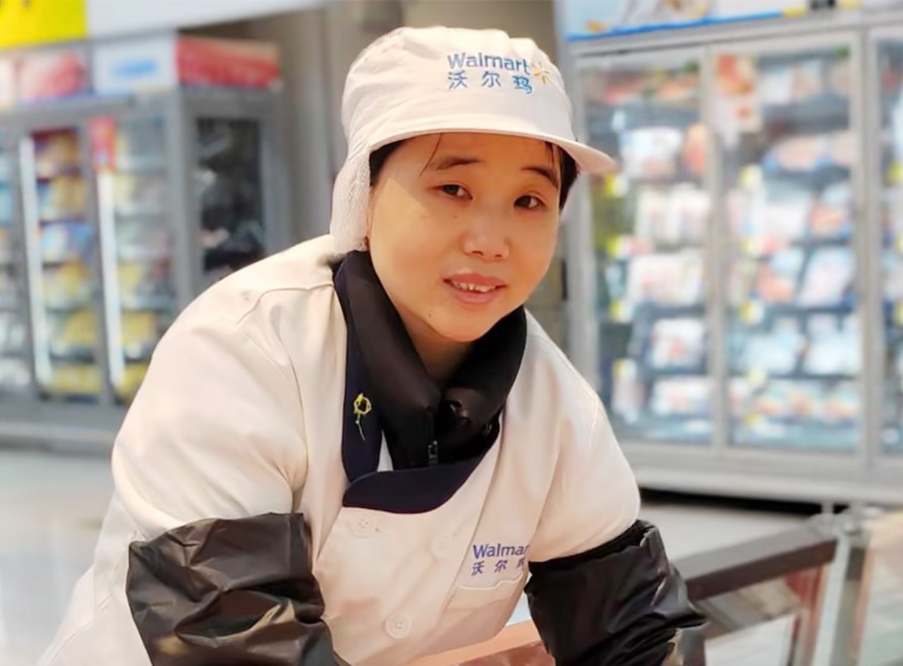 Walmart associate Deng Jin smiles and leans over refrigerated case.