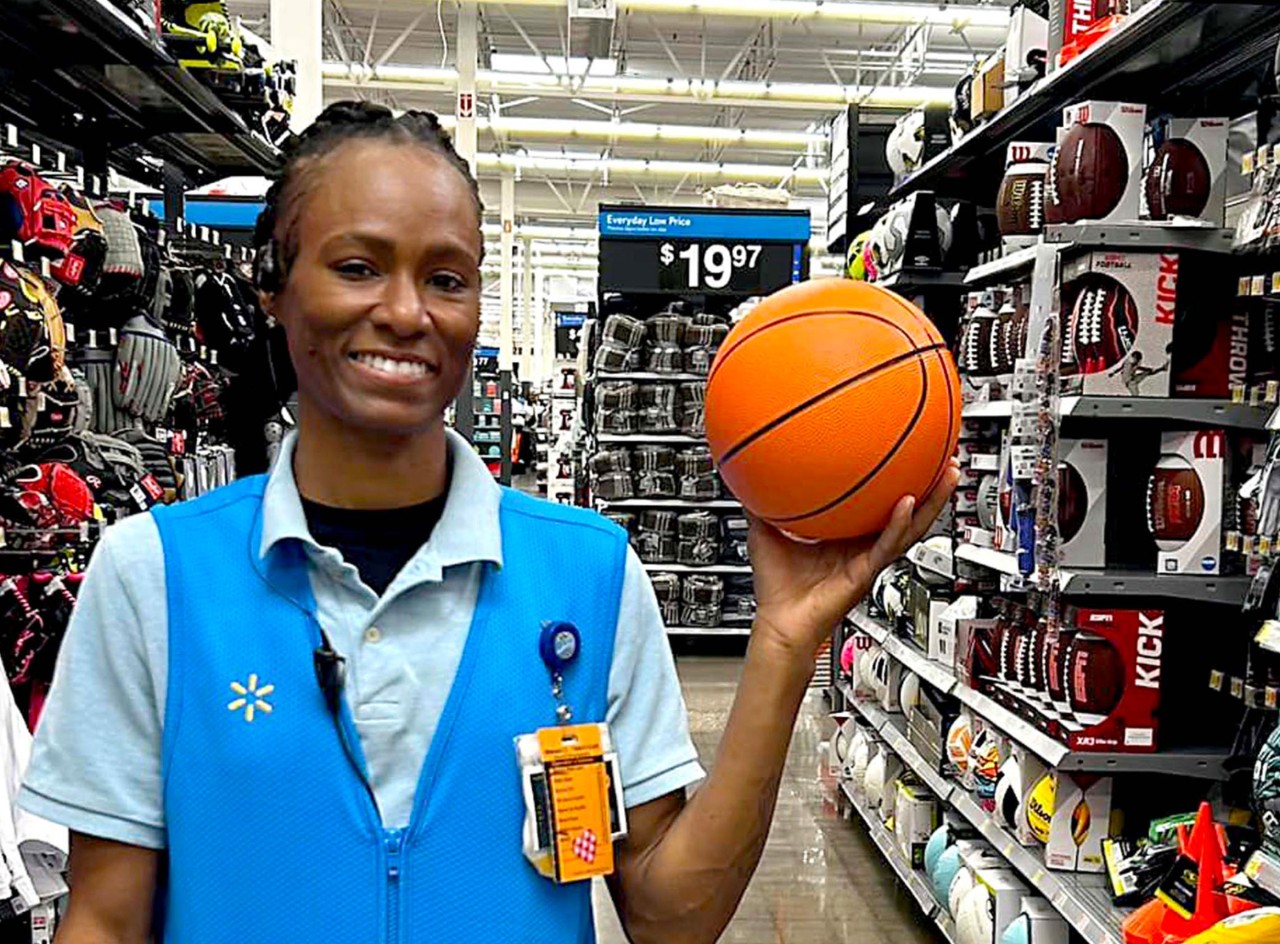 Stocking 2 Team Lead and former WNBA player Crystal Smith smiles, holding up a basketball in an aisle of her Walmart store.