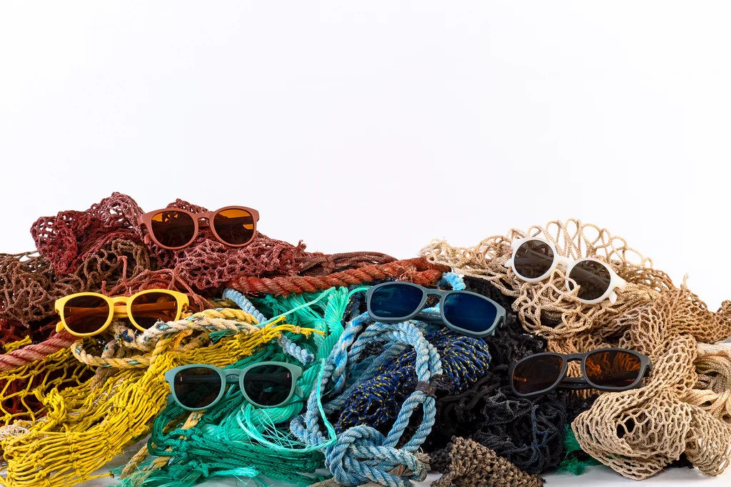 Multiple brightly colored pairs of Karun sunglasses displayed in tangles of matching colored nets, against a white background.